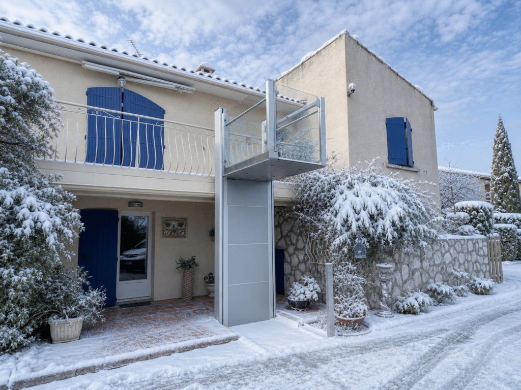 All-weather outdoor vertical platform lift installed on a residential house balcony in winter snow